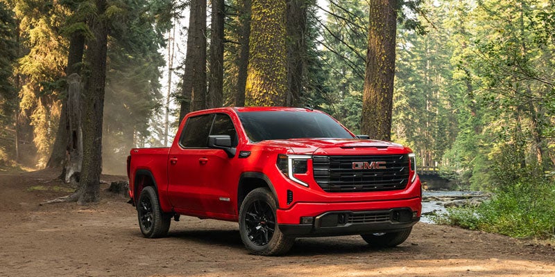 Red GMC Sierra pickup truck parked on a forest trail near a river.